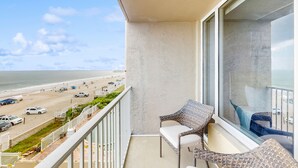 A balcony with wicker furniture overlooking a beach with vehicles and people.