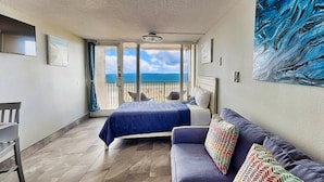 A balcony with a bed and a sofa, a view of the sea, and a painting on the wall.