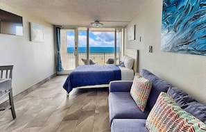 A balcony with a bed and a sofa, a view of the sea, and a painting on the wall.
