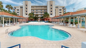 Ein Swimmingpool, umgeben von Liegestühlen, mit einem großen Hotelgebäude und mehreren Etagen sowie Balkonen.