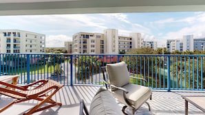 Ein Balkon mit zwei Loungestühlen, einem Tisch und Blick auf ein Wohngebiet mit mehreren Gebäuden und einem grünen Park.