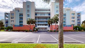 A multi-story hotel with a central entrance, surrounded by parking spaces and palm trees.
