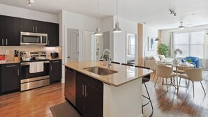 A modern kitchen with dark cabinets, stainless steel appliances, and a central island with a sink. - Elegant 2B Near Legacy West Wi-fi, Fitness, Pool (Frisco)