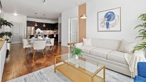 A modern living room with a glass coffee table, a sofa, and a dining area with chairs. - Elegant 2B Near Legacy West Wi-fi, Fitness, Pool (Frisco)