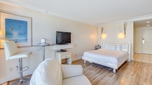 Ein modernes Hotelzimmer mit Bett, Schreibtisch mit Fernseher, weißem Stuhl und einem Bild an der Wand.