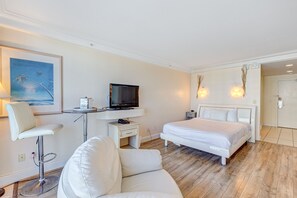 A modern hotel room with a bed, a desk with a TV, a white chair, and a painting on the wall. - Daytona Beach Resort 719 (Daytona Beach)