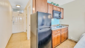 A compact kitchen with wooden cabinets, a black refrigerator, and a microwave. - Pirates Cove 618 - Sunshine Serenity (Daytona Beach Shores)