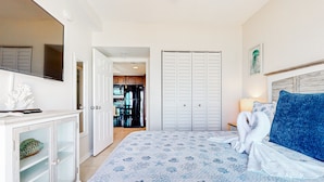 A bedroom with a bed, a TV, a wardrobe, and a bathroom visible through an open door. - Coconut Palms Beach Resort 4312 (New Smyrna Beach)