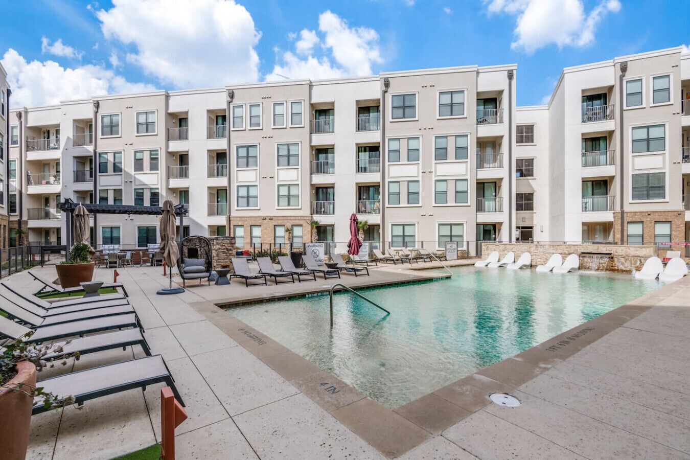 A modern hotel with a swimming pool, lounge chairs, and a patio area.