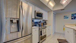 Una cocina moderna con electrodomésticos de acero inoxidable, armarios blancos y suelo de baldosas.