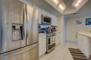 A modern kitchen with stainless steel appliances, white cabinetry, and a tiled floor. - Dimucci Twin Towers 404 - Ocean Oasis (Daytona Beach Shores)