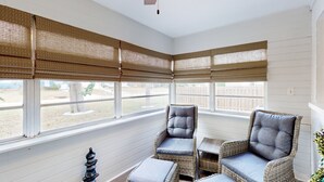 Un solarium con mobiliario de mimbre, ventanas amplias con persianas y un ventilador de techo.