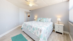 A bedroom with a bed, nightstands, a ceiling fan, and a green rug. - Southpoint 303 (Ponce Inlet)