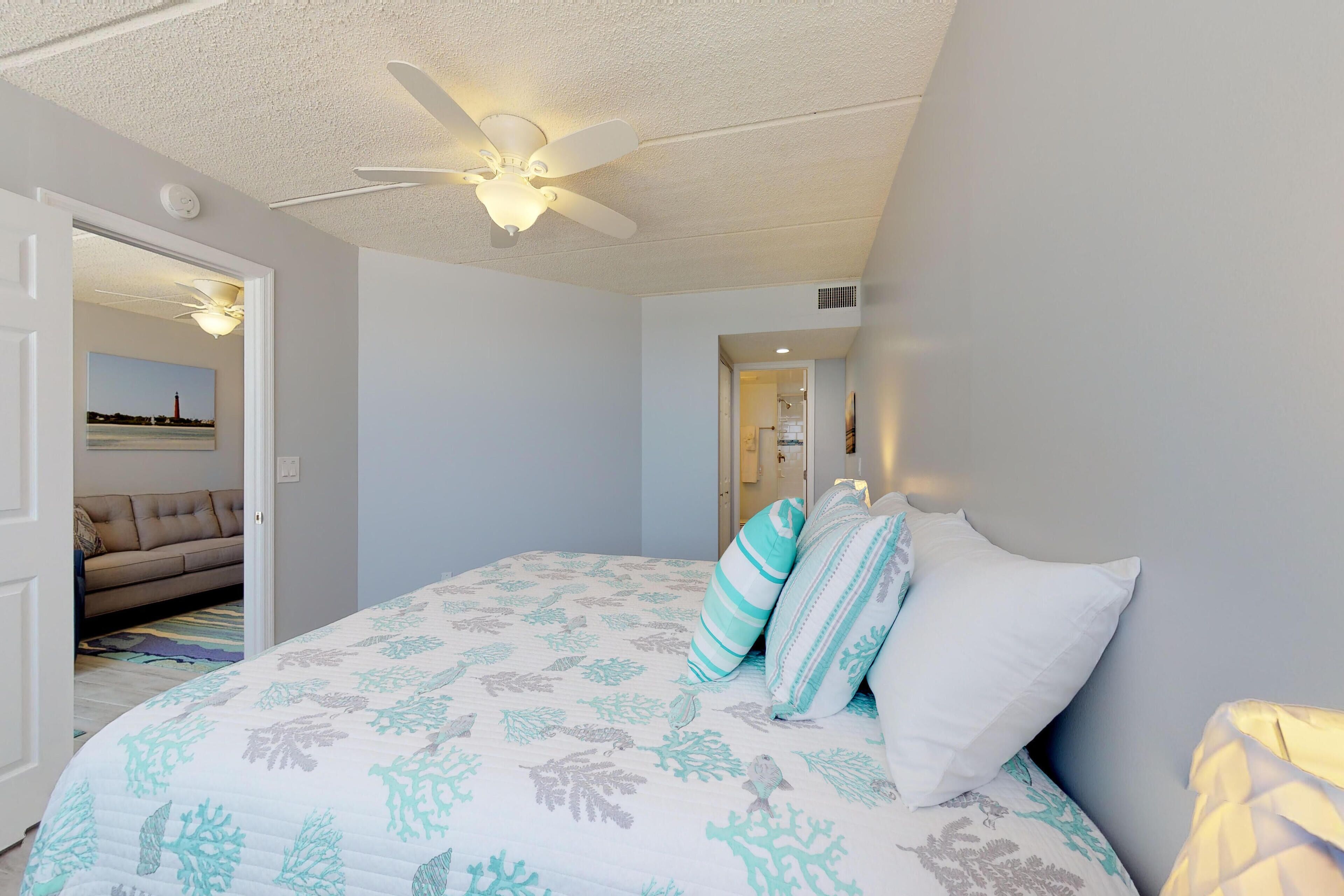 A bedroom with a bed, a ceiling fan, and a view of another room with a couch.