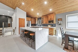 A modern kitchen with a marble island, wooden cabinets, and a dining area with a dark wooden table and chairs. - Spacious Park City Retreat With a Private Hot Tub (Park City)