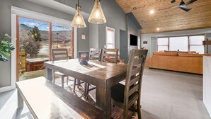 Un'ampia zona pranzo con tavolo e sedie in legno, una grande finestra vista all'esterno e una ventola a soffitto.