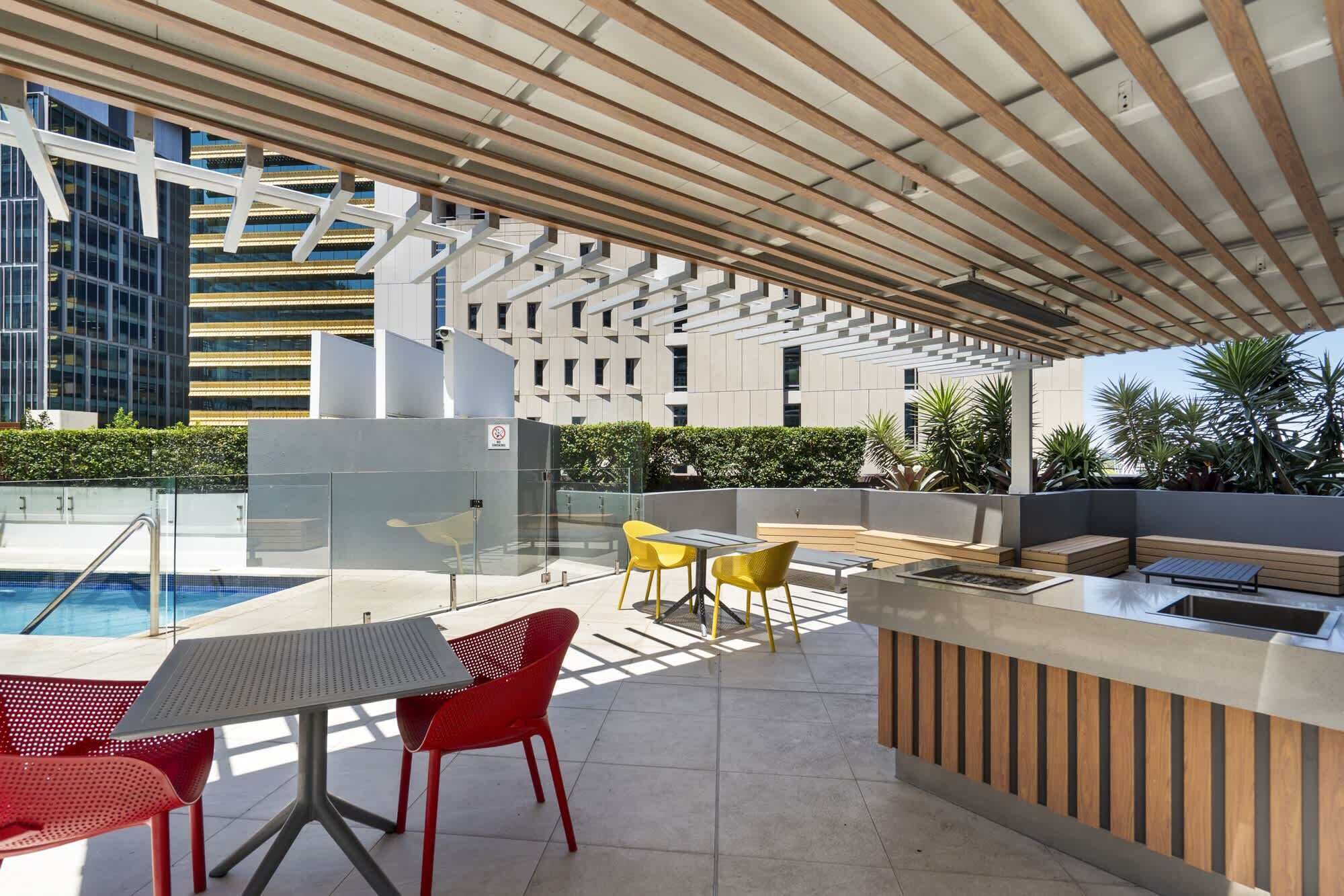 An outdoor pool area with a covered seating area, tables, and chairs.