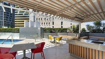 An outdoor pool area with a covered seating area, tables, and chairs.
