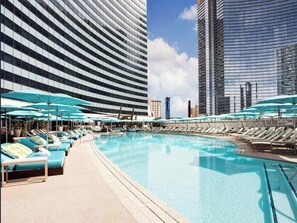 Ein Poolbereich mit Liegestühlen und Sonnenschirmen, umgeben von modernen Hochhäusern.