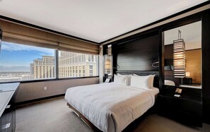A modern hotel room with a large bed, a desk, and a view of city buildings. - Luxe Vdara High-floor Panoramic Strip Views Sphere Views 22032 (Las Vegas)