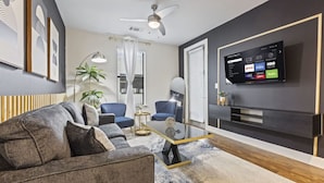 A modern living room with a grey sofa, blue armchairs, a coffee table, and a flat-screen TV mounted on the wall. - Great for Children 2 Bedroom With Bunk Beds (Frisco)