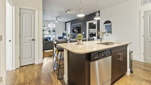 A modern kitchen with a central island, stainless steel appliances, pendant lighting, and a view into the living area. - Great for Children 2 Bedroom With Bunk Beds (Frisco)