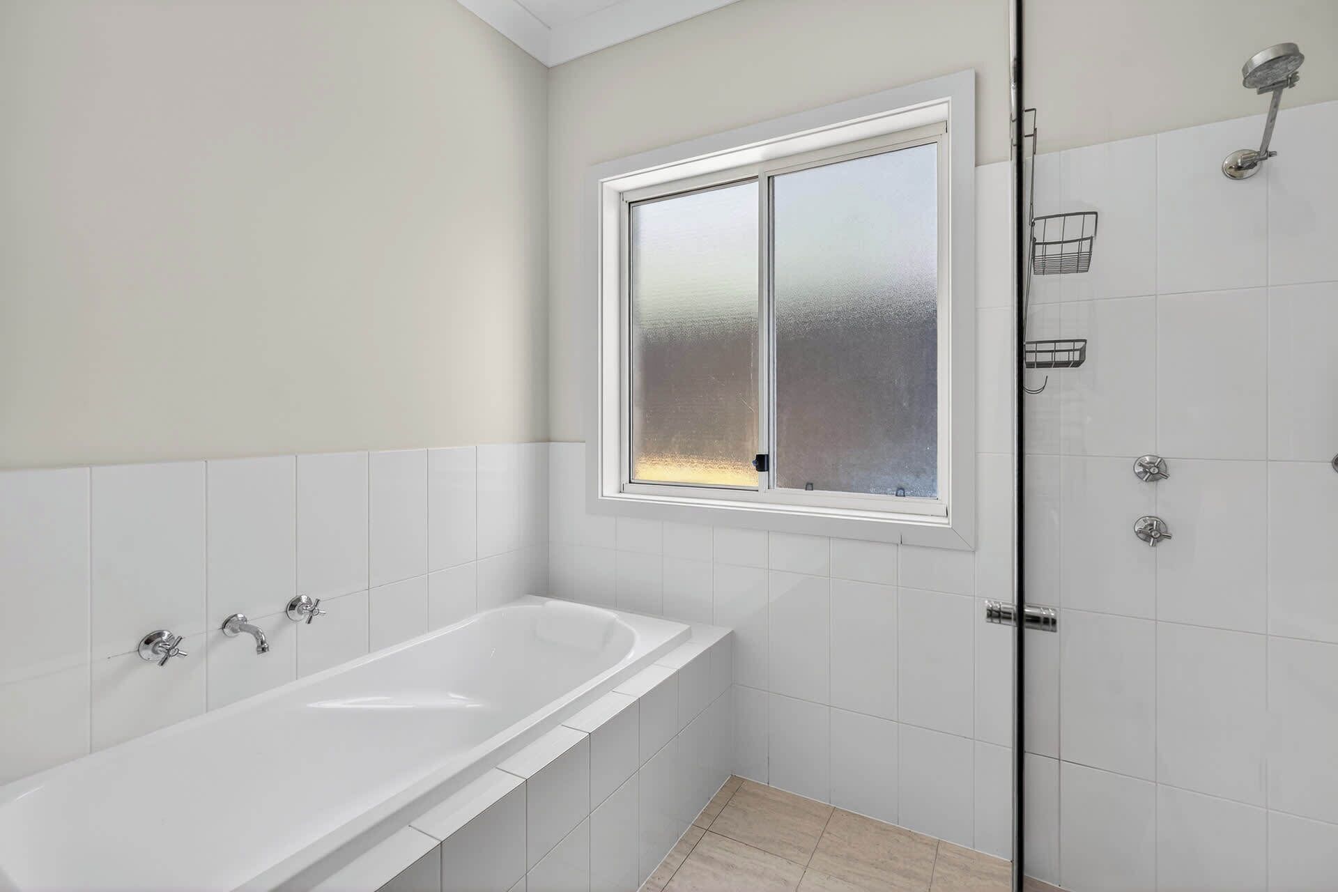 A bathroom with a bathtub, a shower, and a frosted window.