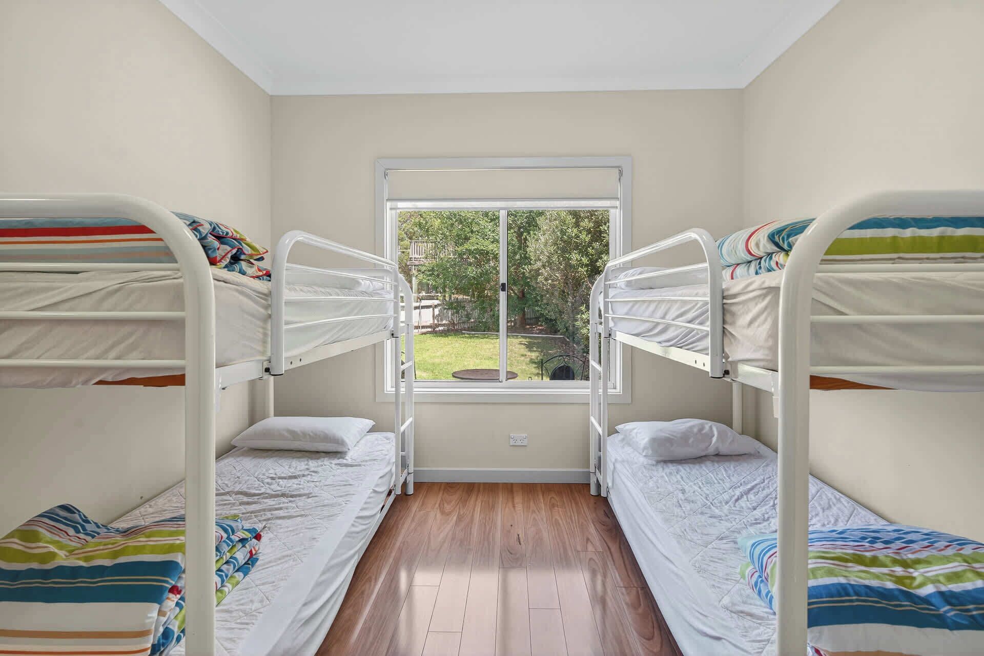 Une chambre avec deux lits superposés, une fenêtre donnant sur un paysage verdoyant et un plancher en bois.