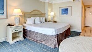 Una habitación de hotel con una cama grande, dos mesitas de noche con lámparas, una mesita con teléfono y una pequeña mesa con una silla.