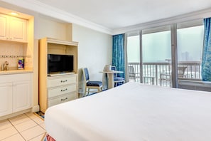 Ein Hotelzimmer mit Bett, Fernseher, Schreibtisch mit Schubladen, Stuhl, kleinem Tisch und einem Balkon mit Aussicht.