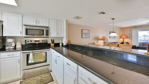 A kitchen with white cabinets, a stainless steel oven, a microwave, and a granite countertop. - Twenty-six Twenty-six 202 - Shores Delight (Daytona Beach)