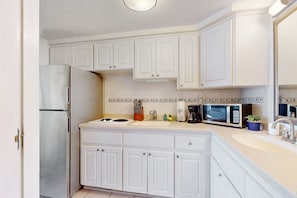 A kitchen with white cabinets, a stainless steel refrigerator, a microwave, and a sink. - Daytona Beach Resort 406 (Daytona Beach)