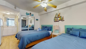 Een slaapkamer met twee bedden, een plafondventilator, een spiegel en een muur met decoraties van zeilboten.