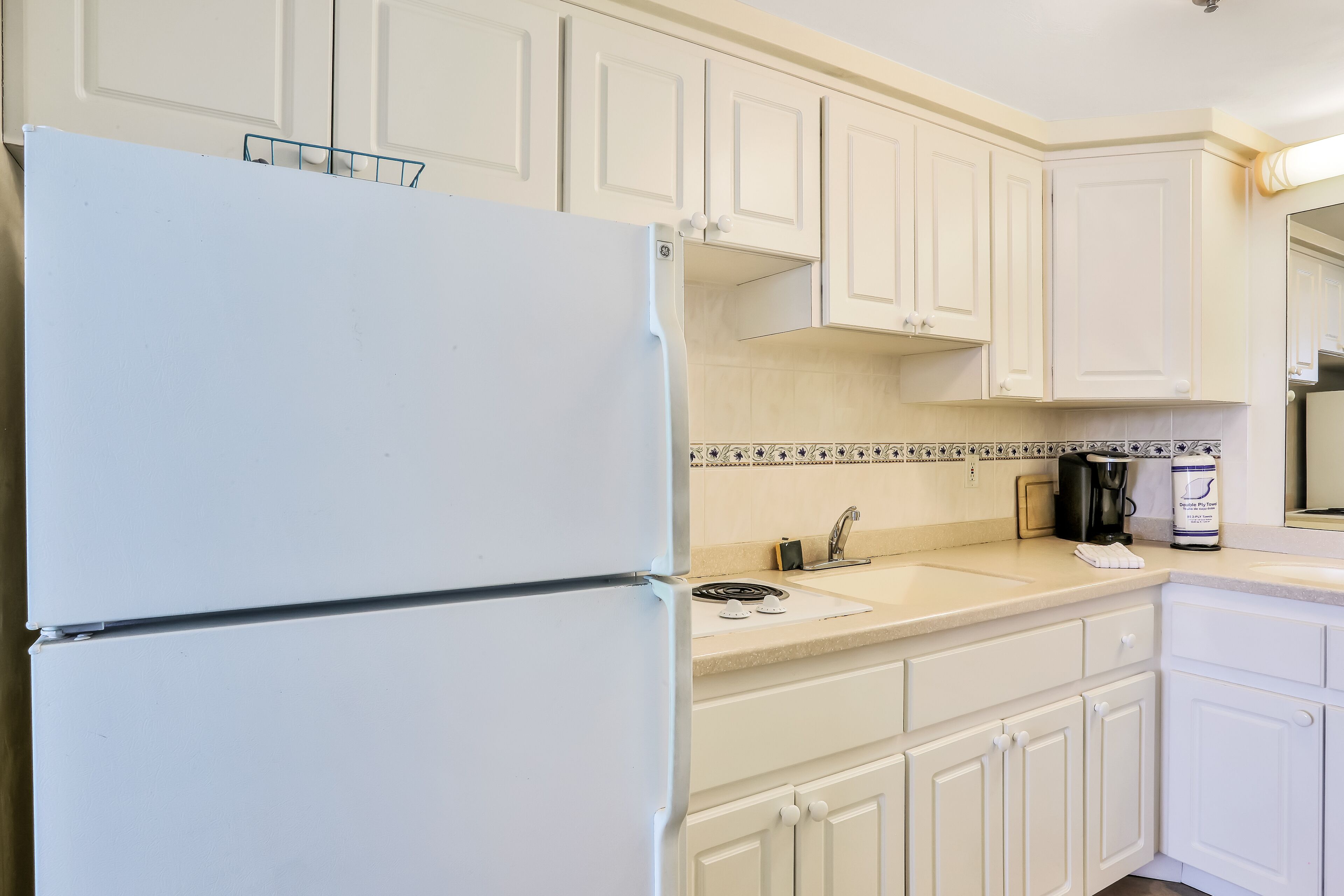A kitchen with white cabinets, a white refrigerator, a double sink, and a coffee maker.