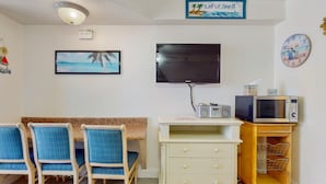 Een kamer met een televisie, een magnetron, een klein kastje en een zithoek met stoelen.