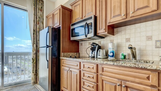 A kitchen with wooden cabinets, a stainless steel microwave, and a refrigerator. - Daytona Beach Resort 1404 (Daytona Beach)