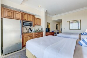 Ein Hotelzimmer mit Küchenzeile, zwei Betten und einem durchgegangenen Tür sichtbaren Badezimmer.