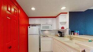 A compact kitchen with white cabinets, a white refrigerator, a microwave, and a sink. - Daytona Beach Resort 801 (Daytona Beach)