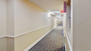 A hotel hallway with carpeted floors, white walls, and a fire exit sign. - Daytona Beach Resort 801 (Daytona Beach)