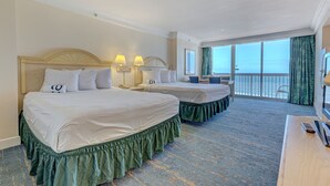 Habitación de hotel con dos camas, un escritorio con televisor y un balcón con vistas.