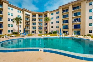 A swimming pool surrounded by a multi-story building with balconies, lounge chairs, and palm trees. - Twenty-six Twenty-six 406 - Bright Delight (Daytona Beach)
