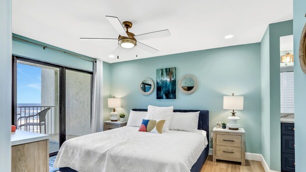 A bedroom with a bed, bedside tables, a ceiling fan, and a view of the outdoors.