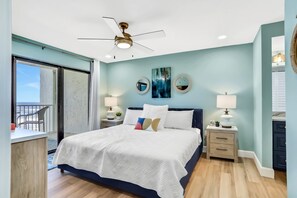 Une chambre à coucher avec un lit, des tables de chevet, un ventilateur de plafond et une vue sur l’extérieur.