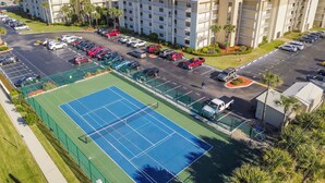 A multi-story hotel with a parking lot and a tennis court.
