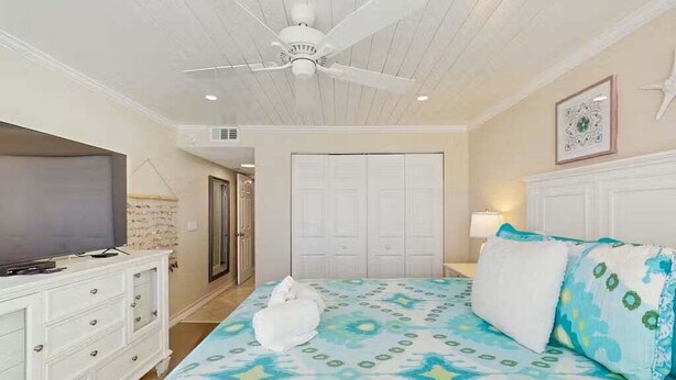 A bedroom with a bed, a television on a dresser, a ceiling fan, and a door. - Point East 302 -just Beachy (New Smyrna Beach)