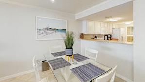 A dining area with a glass table, white chairs, and a potted plant. - Point East 302 -just Beachy (New Smyrna Beach)