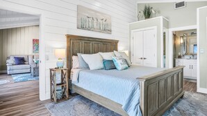 A bedroom with a wooden bed, a nightstand, a lamp, and a painting on the wall. - Sea Dunes A1- Dream Catcher (New Smyrna Beach)
