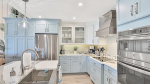 A modern kitchen with light blue cabinets, stainless steel appliances, and a marble countertop. - Sea Dunes A1- Dream Catcher (New Smyrna Beach)