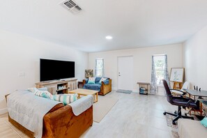 A living room with a flat-screen TV, a sofa, a coffee table, and a dining area with chairs. - Tropical Haven Retreat (Palm Bay)