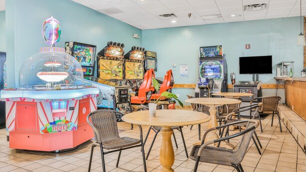 Ein hell erleuchteter Arcade-Bereich mit verschiedenen Spielautomaten, einer Ticketerlassschneide und mehreren Tischen und Stühlen zum Sitzen.